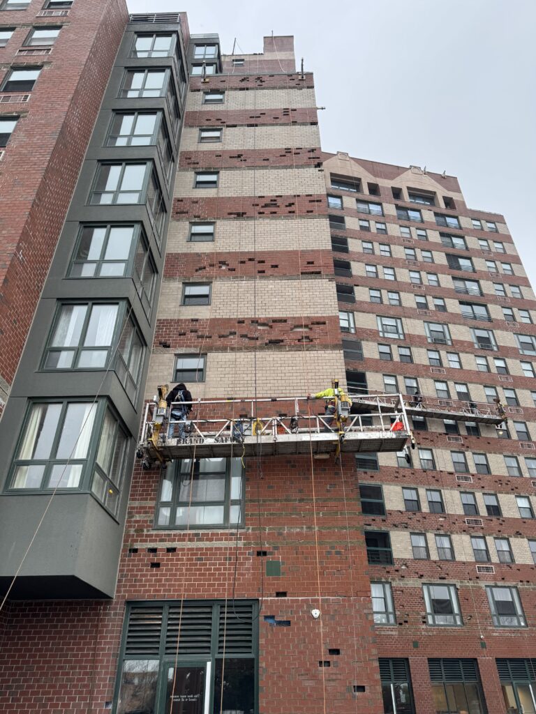 Crew on a swing stage replacing damaged brick during brick restoration on a high-rise